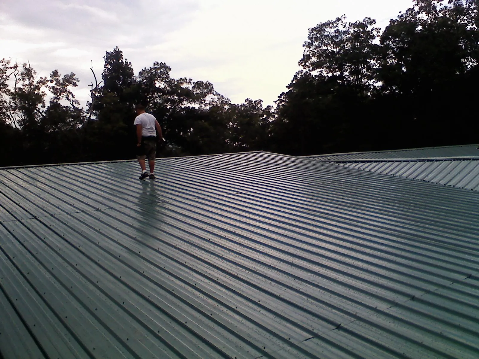 Roofer walking a wide expanse of new green metal roofing in Diamond