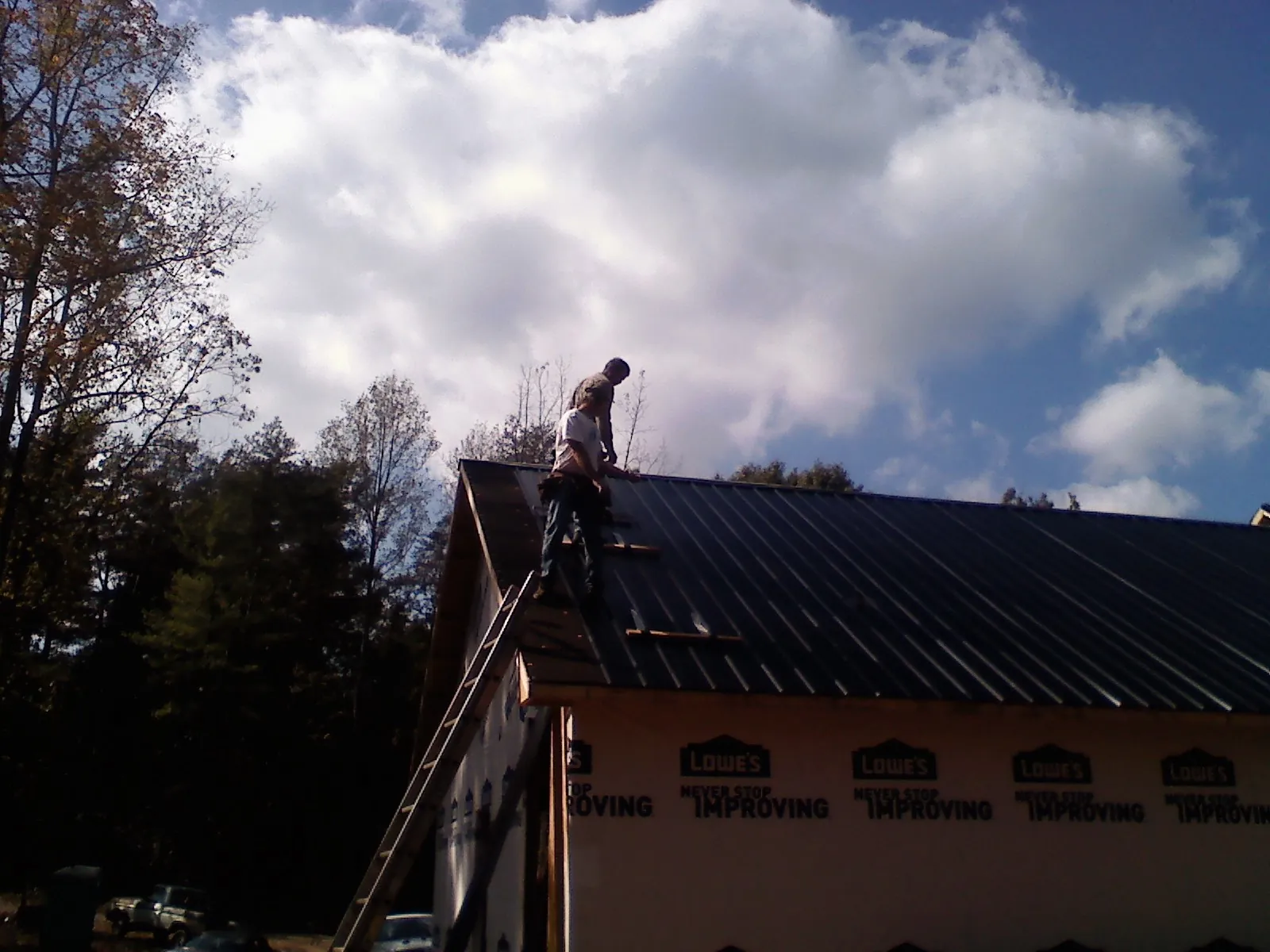 Roofer fastening dark metal panels high against a cloudy sky, from a Roof Inspection job in Diamond